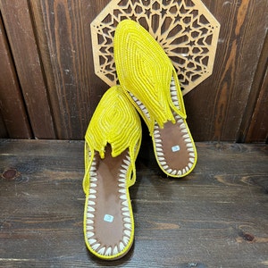 May include: A pair of yellow woven leather slippers with white stitching. The slippers have a pointed toe and a flat sole.