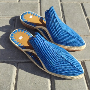 May include: A pair of blue woven leather slippers with a pointed toe and a cream-coloured trim. The slippers are made of a woven material and have a leather sole.