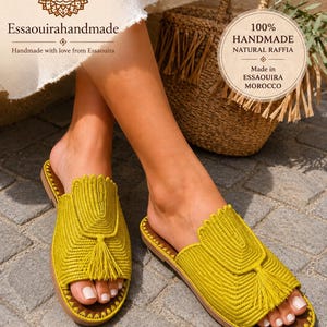 May include: Yellow raffia slide sandals with a tassel detail. The sandals have a brown sole and are handmade. The image includes the text "Essaouirahandmade" and "100% Handmade Natural Raffia Made in Essaouira Morocco".