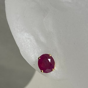 May include: A pair of ruby earrings with a gold setting. The ruby is a deep red colour and is oval shaped.