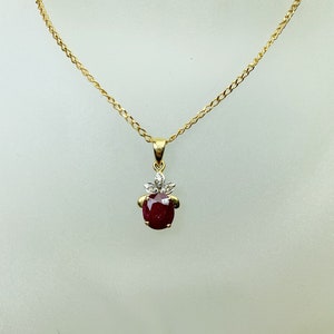 Op de afbeelding: Een gouden ketting met een hanger met een rode robijn-edelsteen omringd door kleinere diamanten.