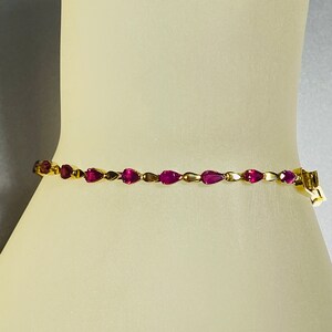May include: A gold bracelet with a row of pink pear-shaped gemstones.