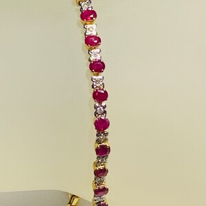 May include: A gold bracelet with alternating red rubies and white diamonds. The bracelet is made of 14k gold and features a classic tennis chain design.