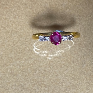 Könnte beinhalten: Ein goldener Ring mit einem rosafarbenen ovalen Edelstein, der von kleineren klaren Edelsteinen umgeben ist.