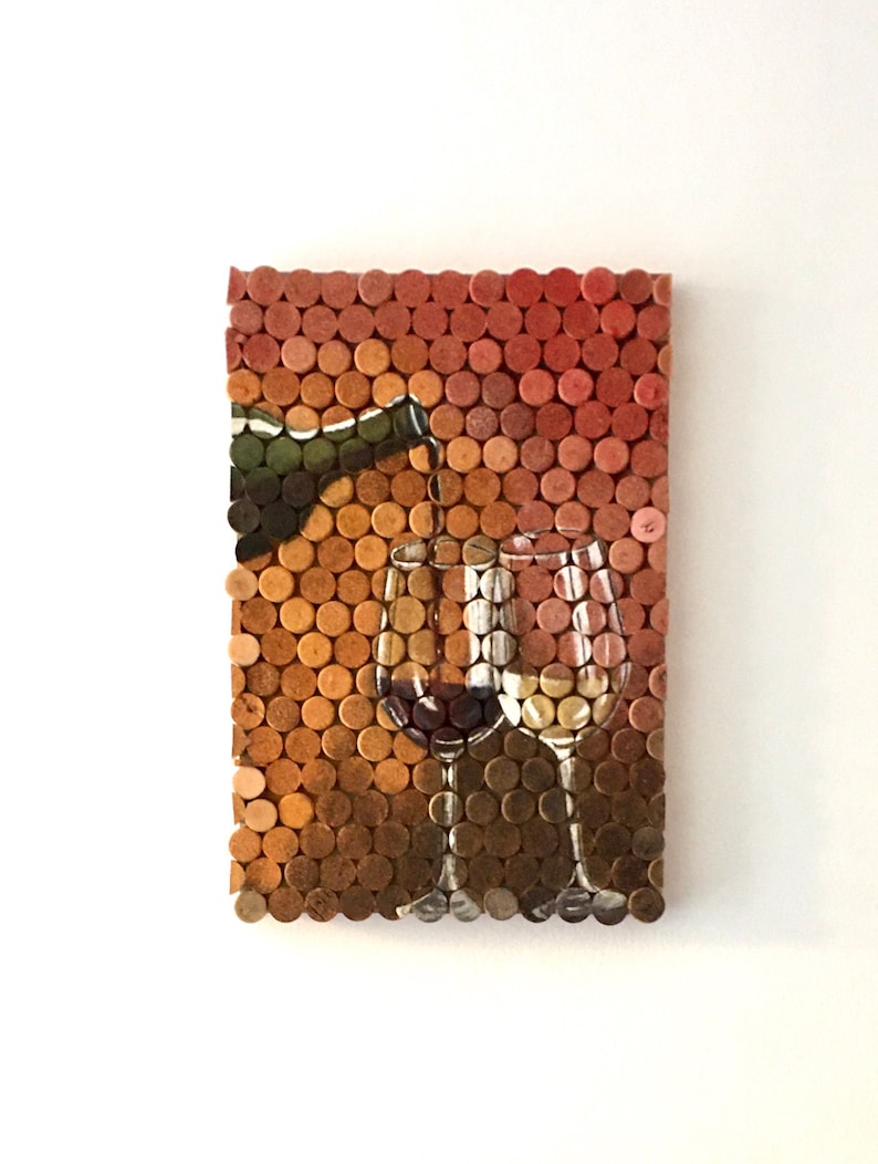 Puede incluir: Una obra de arte de pared hecha de corchos de vino, que representa una botella de vino vertiendo vino en dos vasos. Los corchos est&aacute;n dispuestos en una cuadr&iacute;cula, creando un efecto de mosaico. Los colores de los corchos van del marr&oacute;n claro al marr&oacute;n oscuro, con algunos tonos rojos y naranjas.
