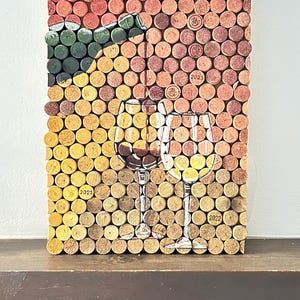 Puede incluir: Una obra de arte de pared hecha de tapones de vino, con dos copas de vino y una botella de vino. Los tapones est&aacute;n dispuestos en un patr&oacute;n de cuadr&iacute;cula y tienen diferentes tonos de marr&oacute;n y rojo. Los a&ntilde;os 2022, 2023 y 2025 est&aacute;n impresos en algunos de los tapones.
