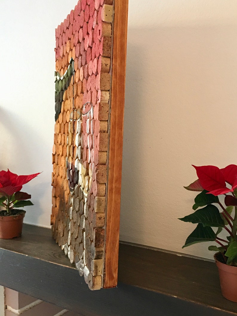 Puede incluir: Una obra de arte enmarcada hecha de corchos de vino, dispuestos en un patr&oacute;n de mosaico. La obra de arte presenta una variedad de colores, incluyendo rojo, naranja y marr&oacute;n. El marco est&aacute; hecho de madera y tiene un acabado natural.