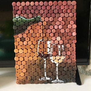 Puede incluir: Una pieza de arte de pared hecha de tapones de vino, que representa una botella de vino y dos vasos. Los tapones est&aacute;n dispuestos en un patr&oacute;n de cuadr&iacute;cula y pintados con pintura marr&oacute;n, roja y blanca.