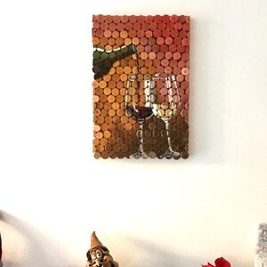 Puede incluir: Una pieza de arte de pared hecha de corchos de vino, que representa una botella vertiendo vino en dos vasos. Los corchos est&aacute;n dispuestos en un patr&oacute;n de cuadr&iacute;cula y pintados con una representaci&oacute;n realista del vino.