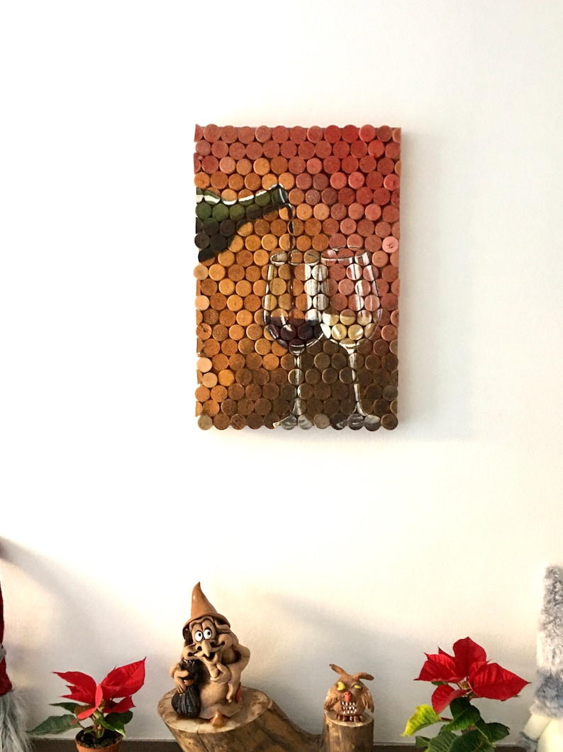 Puede incluir: Una pieza de arte de pared hecha de corchos de vino, que representa una botella vertiendo vino en dos vasos. Los corchos est&aacute;n dispuestos en un patr&oacute;n de cuadr&iacute;cula y pintados con una representaci&oacute;n realista del vino.