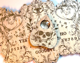 May include: A wooden Ouija board with a skull and floral design planchette. The board features a traditional alphabet, numbers, yes, no, and goodbye.
