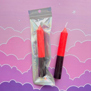 Könnte beinhalten: Zwei rote und schwarze Kerzen in einer durchsichtigen Plastiktüte. Die Kerzen sind etwa 15 cm lang.