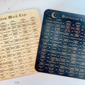 May include: Two wooden boards with a diamond pattern. The boards are labeled "Shadow Work Cast" and "Divination Casting". Each board has a grid of words related to the respective theme.