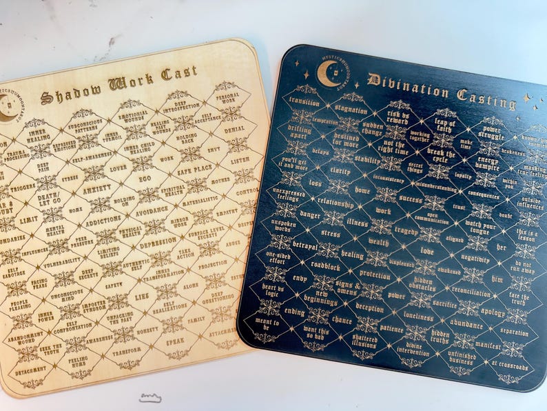 May include: Two wooden boards with a diamond pattern. The boards are labeled "Shadow Work Cast" and "Divination Casting". Each board has a grid of words related to the respective theme.