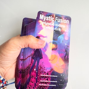 Puede incluir: Una baraja de cartas de oráculo Mystic Fusion con un diseño morado, rosa y azul. Las cartas presentan a una mujer con un rostro brillante y un fondo de cielo estrellado. El texto en las cartas dice "Mystic Fusion physical features oracle deck".