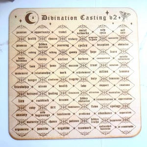 May include: Wooden divination casting board with a grid of words like "passion," "health," and "travel." The board features decorative floral accents and the text "Divination Casting v2+" at the top. A butterfly and crescent moon are also visible.