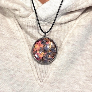 May include: A silver necklace with a round glass pendant filled with dried flowers. The flowers are pink, purple, and yellow.