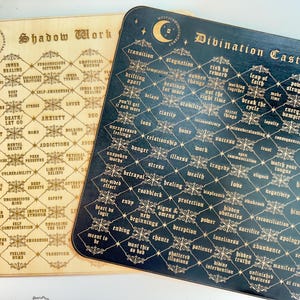 May include: Two wooden divination boards with a black and gold design. The boards are divided into a grid with words and phrases related to shadow work and divination casting. The boards are made of wood and have a distressed finish.