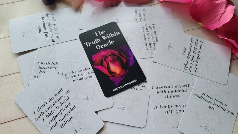 May include: A deck of oracle cards with a black background and a purple and orange rose. The cards are white with black text and feature phrases like "I wish this have work better" and "I distract myself with material things". The text on the top card reads "The Truth Within Oracle".
