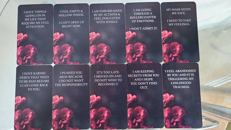 K&ouml;nnte beinhalten: Ein Satz Tarotkarten mit dunklem Hintergrund und floralen Akzenten. Jede Karte zeigt einen anderen Satz in wei&szlig;em Text, wie z. B. "Ich f&uuml;hle mich leer und hohl". Die Karten sind in Reihen angeordnet.