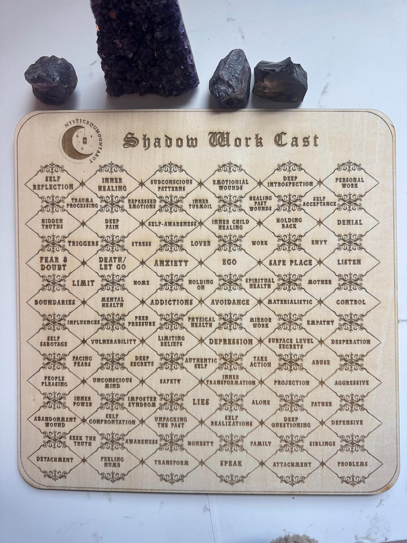 May include: A wooden board with a grid of squares, each containing a word or phrase related to shadow work. The board is titled "Shadow Work Cast".
