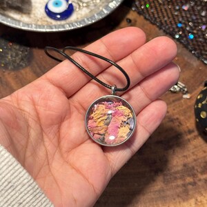 以下が含まれることがあります： ピンクとオレンジの乾燥した花びらで満たされた丸いガラスのチャームが付いたシルバーのペンダントネックレスです。