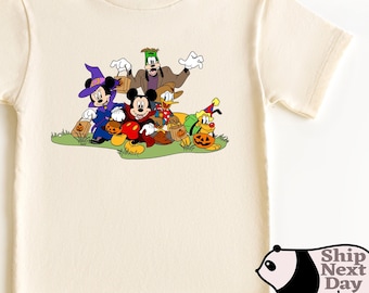 May include: A cream colored t-shirt with a graphic of Mickey Mouse and his friends dressed in Halloween costumes. The graphic includes Mickey Mouse, Minnie Mouse, Donald Duck, Goofy, and Pluto.