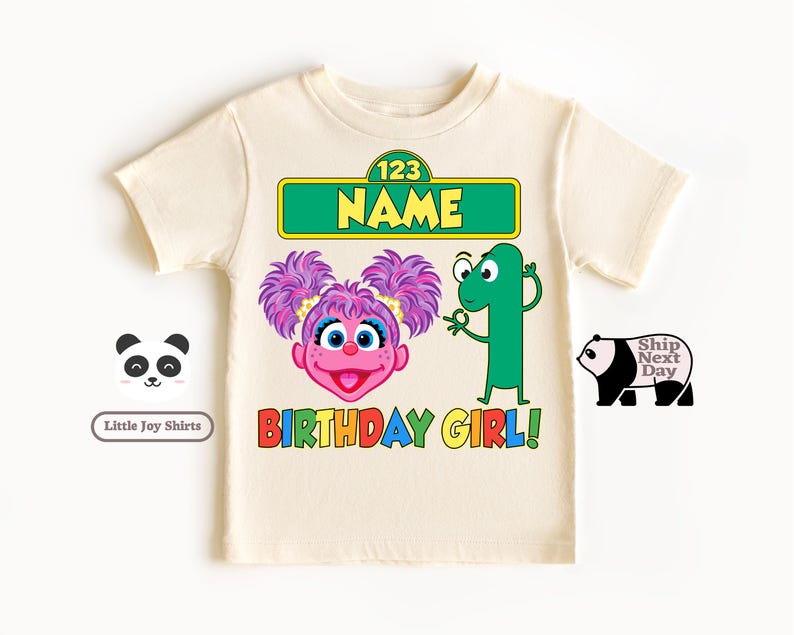 Puede incluir: Camiseta de color crema con un dise&ntilde;o gr&aacute;fico colorido. El dise&ntilde;o incluye un personaje de dibujos animados con pelo morado, el n&uacute;mero 1 y las palabras "BIRTHDAY GIRL!" en colores arco&iacute;ris. La camiseta tambi&eacute;n tiene el texto "NAME".