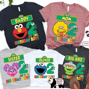 Puede incluir: Varios camisetas coloridas con personajes de Barrio S&eacute;samo y el n&uacute;mero 2. Cada camiseta tiene un dise&ntilde;o diferente, incluyendo "Daddy", "Mom", "Sister", "Oliver" y "Big Bro", con el texto "Of The Birthday Boy!"