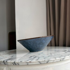 May include: A conical ceramic bowl with a textured, mottled blue exterior and a smooth, dark brown rim. The bowl features a wide, open top that tapers down to a small, circular base, showcasing a handcrafted appearance with subtle colour variations.