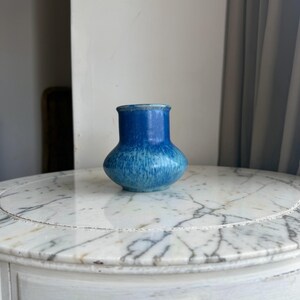 May include: A small ceramic vase with a bulbous base and a narrow neck, featuring a gradient glaze that transitions from a deep, saturated royal blue at the top to a lighter, mottled sky blue and white finish toward the bottom of the vessel.