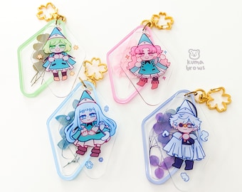 May include: Four clear acrylic charms with cartoon characters in teal and pink outfits, each with a gold-colored flower-shaped clasp. The charms are diamond-shaped with colored borders and include dried flowers. The Kuma Brows logo is visible.