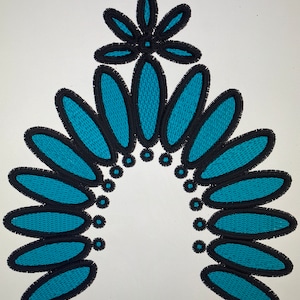 May include: An embroidered design in teal blue and black, featuring a flower at the top and a semi-circular arrangement of oval shapes.