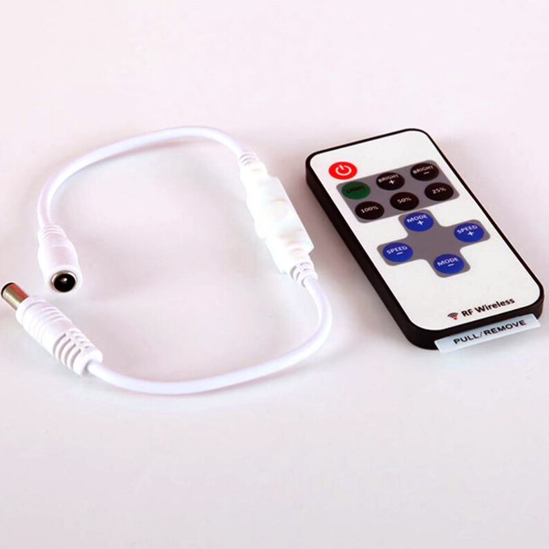 May include: A white remote control with a black face and buttons for controlling LED lights. The remote has buttons for speed, mode, and brightness. The remote also has a button for turning the lights on and off. The remote is connected to a white wire with a power adapter.