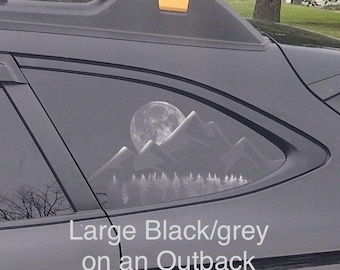 May include: A black Subaru Outback with a large black and grey decal on the rear window. The decal features a mountain range with a full moon in the background.