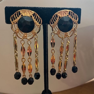 May include: A pair of gold tone dangle earrings with black glass beads and black stones. The earrings have a filigree design.