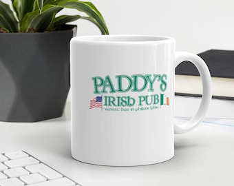 May include: White ceramic mug with a green and white design that says "Paddy's Irish Pub" and "Worst bar in Philadelphia". The mug has a handle on the right side and an American flag and an Irish flag on either side of the text.