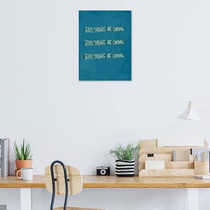 May include: A teal blue canvas print with the text "Good things are coming" repeated three times in white.