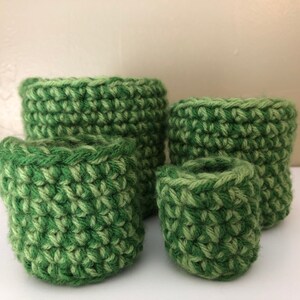 May include: Four green crocheted baskets of varying sizes, stacked on top of each other.