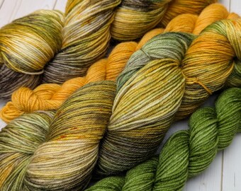 May include: Close-up of several skeins of yarn in various colors. The yarn colors include shades of green, yellow, and brown. The yarn is tightly wound and appears soft, ideal for knitting or crocheting projects.