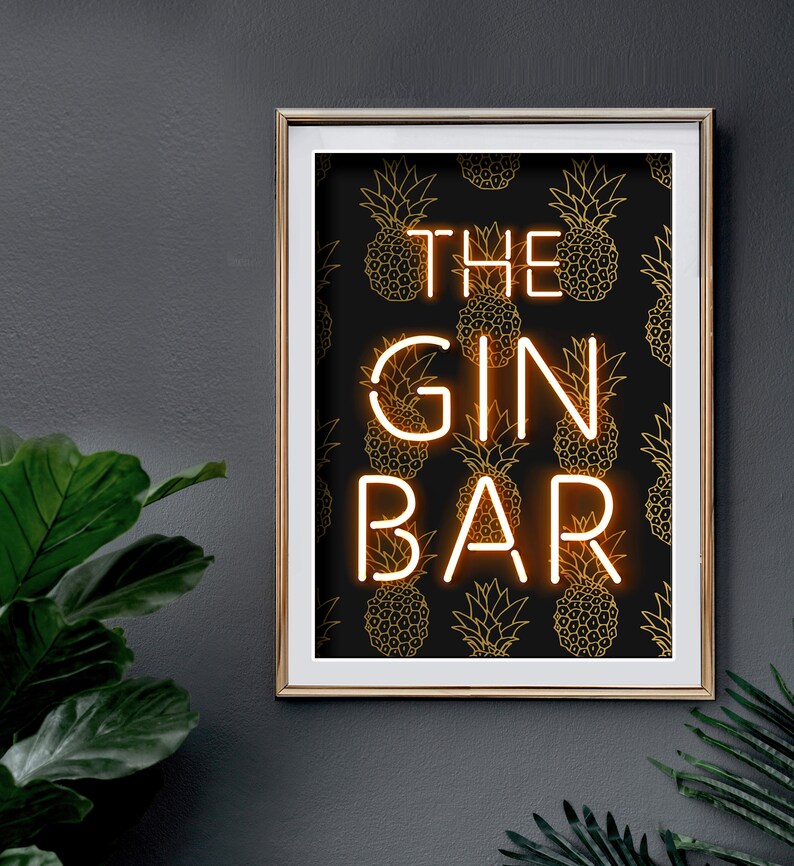 May include: A framed print with a gold border, featuring the words "THE GIN BAR" in a neon-style font. The background is black with a repeating gold pineapple pattern. The print is mounted on a dark gray wall.