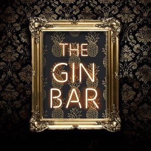 May include: A framed sign with the words "THE GIN BAR" in neon-style lettering. The background features a pattern of gold pineapples on a black background. The frame is ornate and gold, set against a dark, patterned wall.