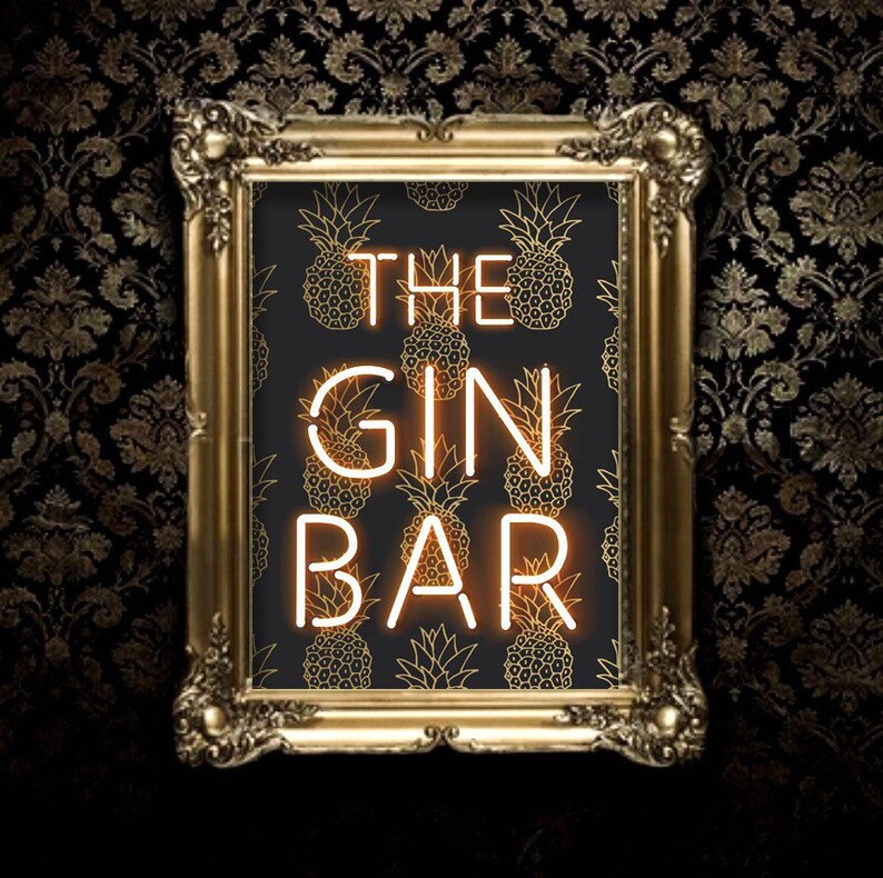 May include: A framed sign with the words "THE GIN BAR" in neon-style lettering. The background features a pattern of gold pineapples on a black background. The frame is ornate and gold, set against a dark, patterned wall.