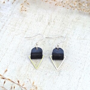 May include: A pair of black leather earrings with gold triangle accents. The earrings are hanging from silver hooks.