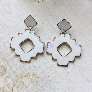 May include: White ceramic earrings with a geometric design. The earrings have a distressed look with a hint of brown paint.
