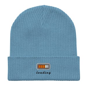 Puede incluir: Un gorro azul claro con textura acanalada. El gorro presenta un diseño bordado de una barra de carga con segmentos naranjas y blancos, y la palabra "loading" en escritura cursiva.