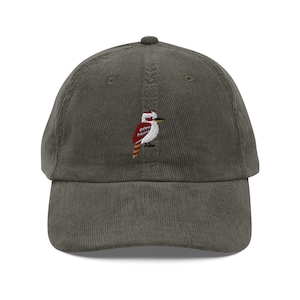 Op de afbeelding: Een groene corduroy baseball cap met een geborduurd ontwerp van een kookaburra vogel. De vogel is afgebeeld in rood, wit en geel. De cap is een klassieke stijl, geschikt voor casual wear. Het vogelontwerp voegt een vleugje natuur toe.