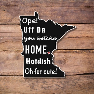 May include: Black and white outline of the state of Minnesota with the text "Ope! Uff Da you betcha HOME. Hotdish Oh fer cute!" inside the outline.