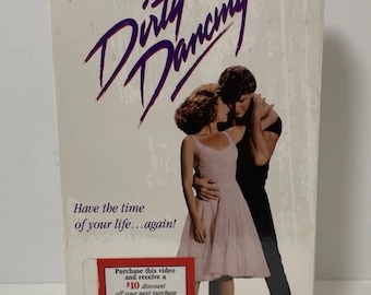 May include: A VHS tape case for the movie Dirty Dancing, featuring Patrick Swayze and Jennifer Grey on the cover. The case is white with purple text and a photo of the actors dancing. The text on the case reads "Dirty Dancing" and "Have the time of your life...again!" There is a small sticker on the bottom right corner of the case that says "Purchase this video and receive a $10 discount off your next purchase of Roses from Flowers U-S-A."