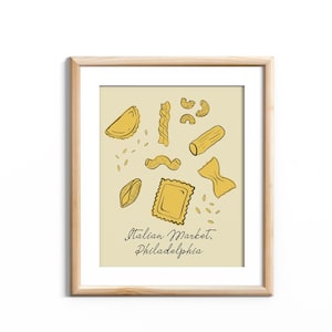 Può includere: Una stampa incorniciata con illustrazioni di diverse forme di pasta in giallo e nero su sfondo beige. Il testo "Italian Market, Philadelphia" è scritto in corsivo sotto i disegni della pasta. La cornice è in legno chiaro.